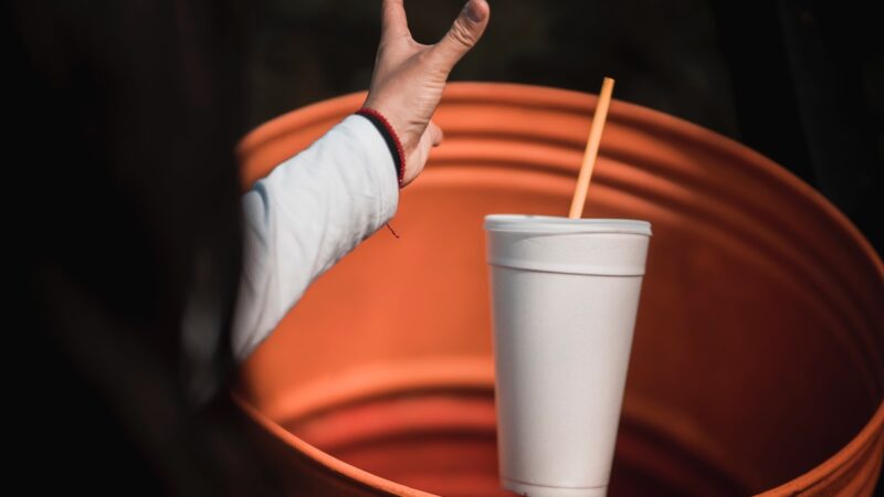 A person throwing away a styrofoam cup into the garbage