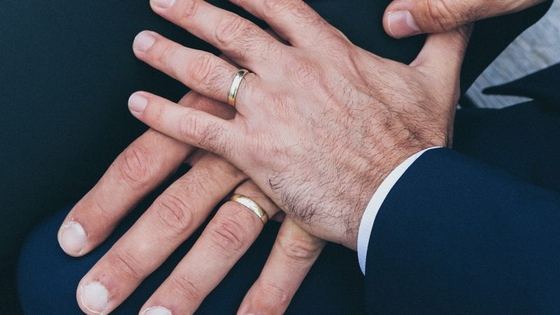 Two men's hands with rings holding each other
