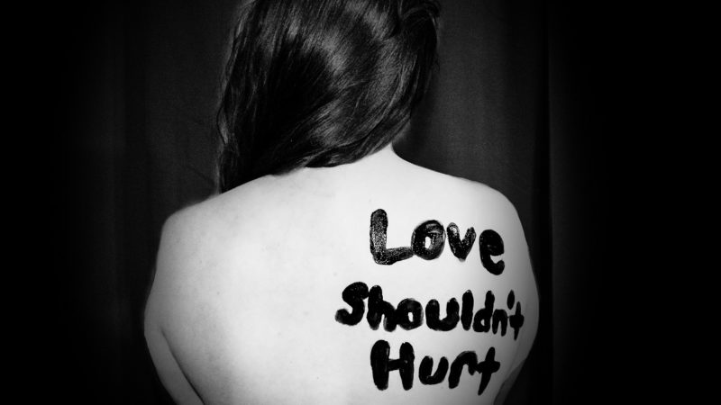 "Love Shouldn't Hurt" written on woman's back
