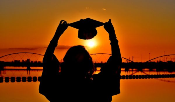 Person holding graduation cap up to sun