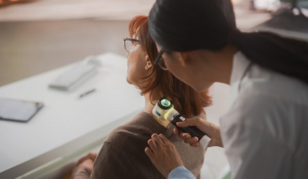 Young Asian Dermatologist is Using a Dermatoscope to Identify Worrying Cancerogenic Tissues on the Skin of a Senior Female