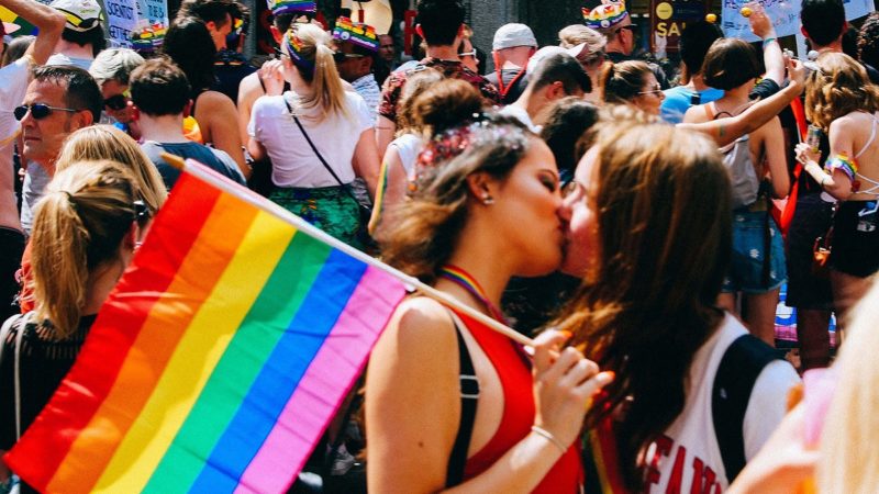 Two women kissing, one holding a LGBTQ pride flag