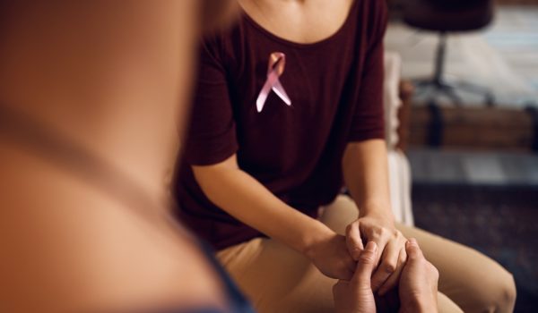 Woman with breast cancer pin holding hands with another